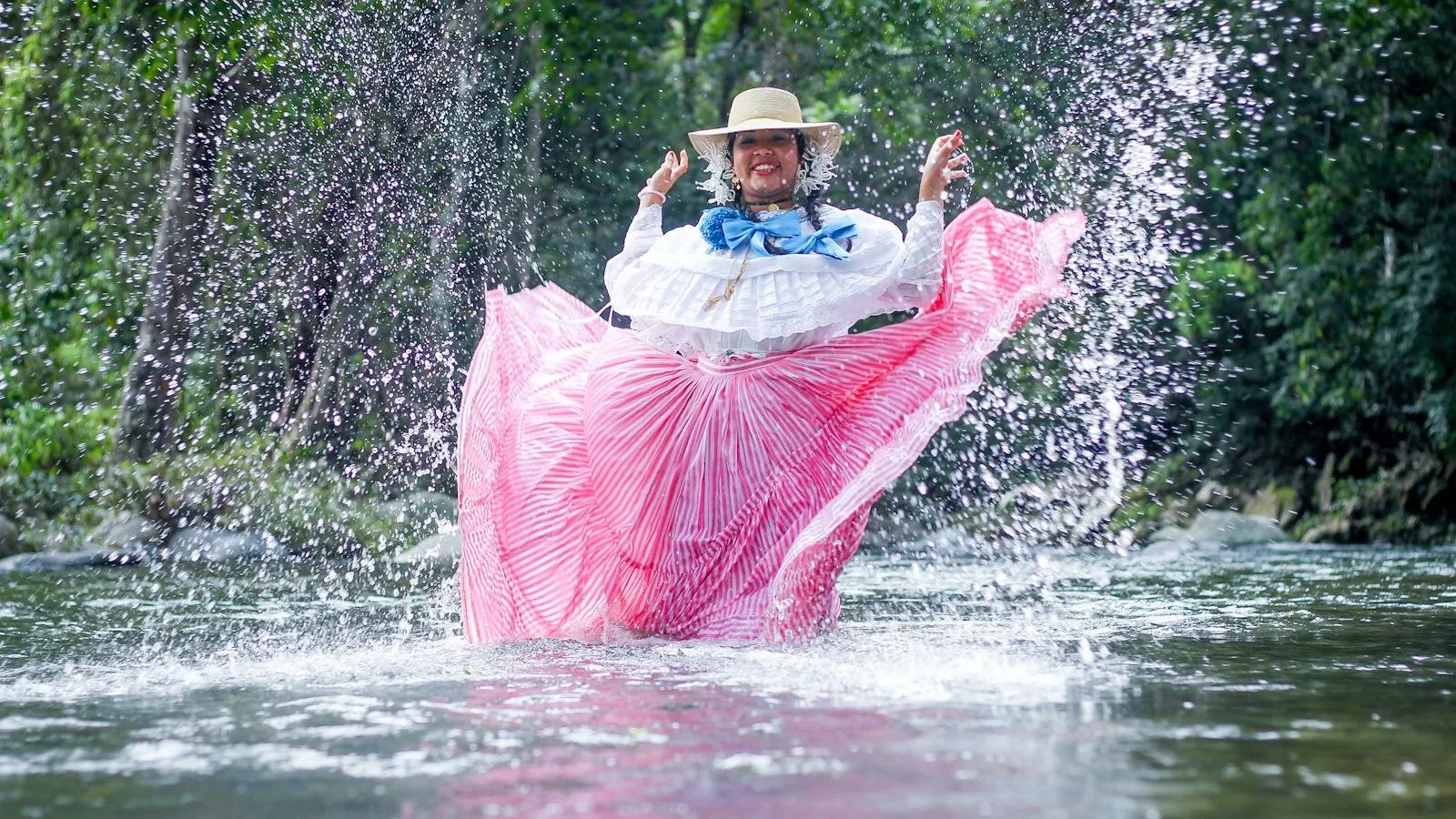 Woman in a pink pollera skirt splashing in a river in Panama